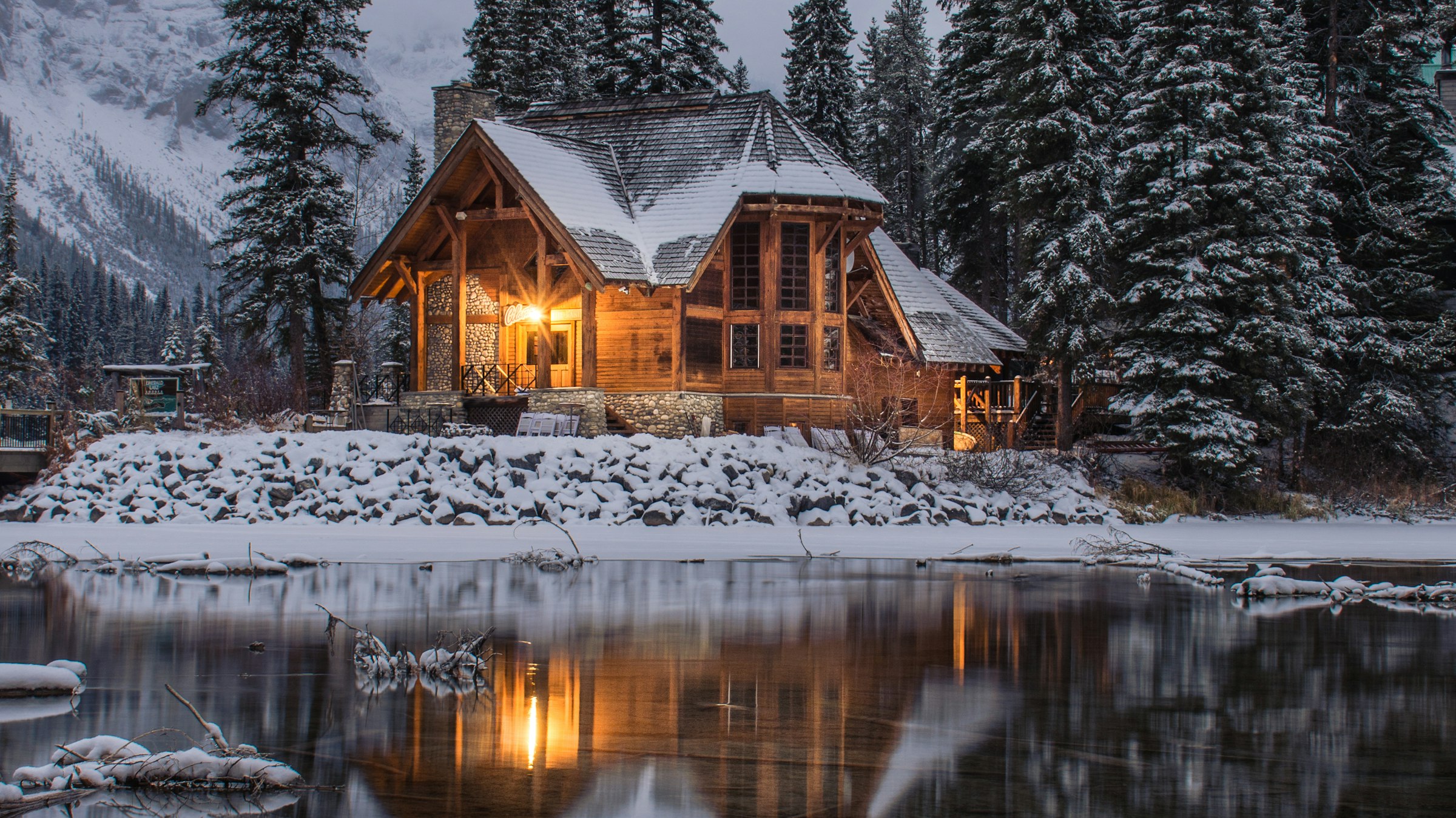 Timber house lit from within beside a frozen lake at dusk