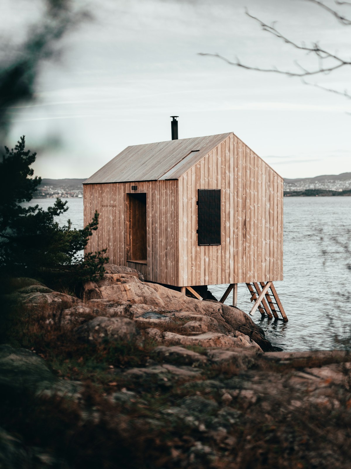 Timber-clad prefabricated cabin raised on stilts above a rocky shoreline
