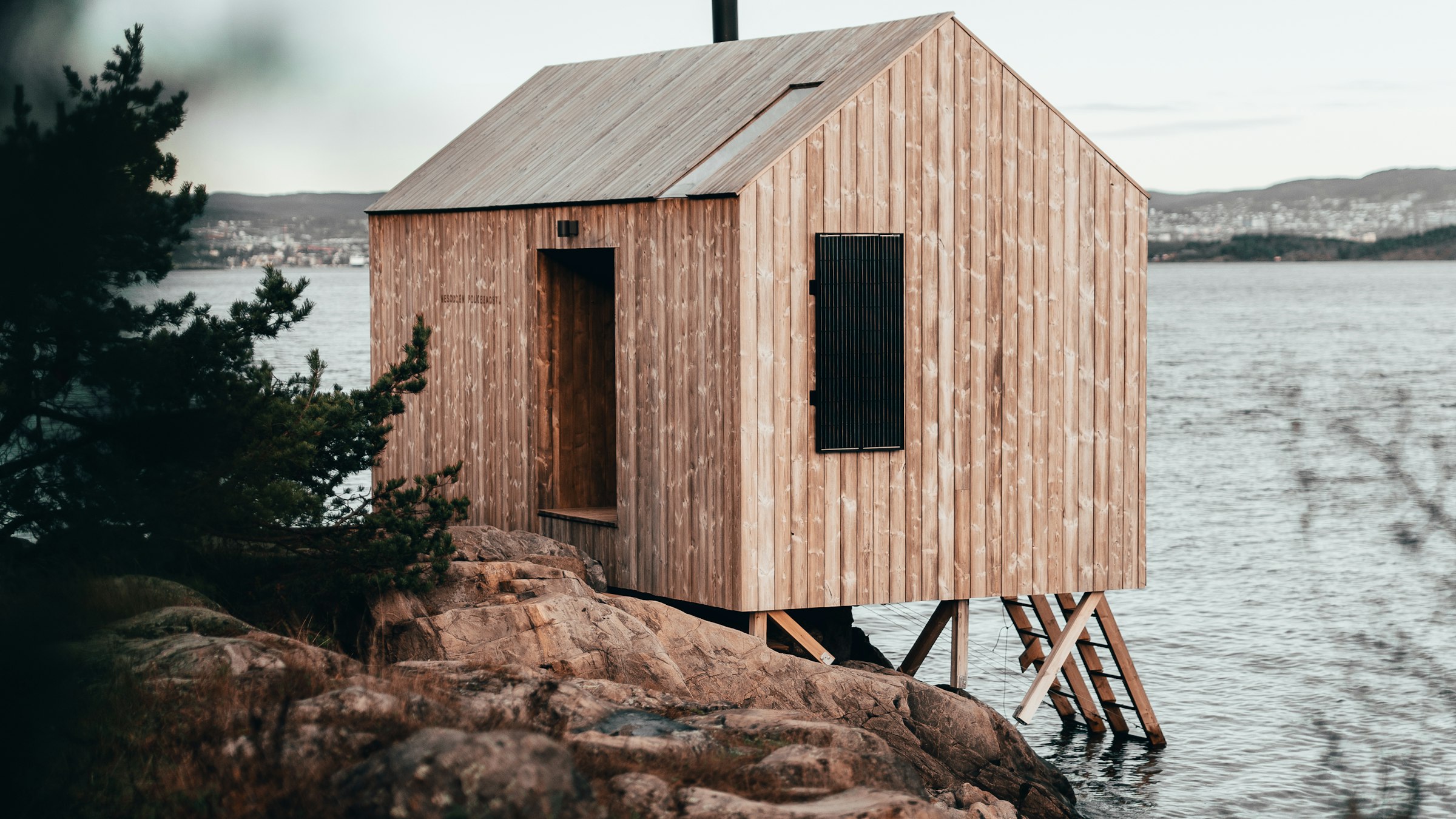 Timber-clad prefabricated cabin standing on stilts over a granite shoreline